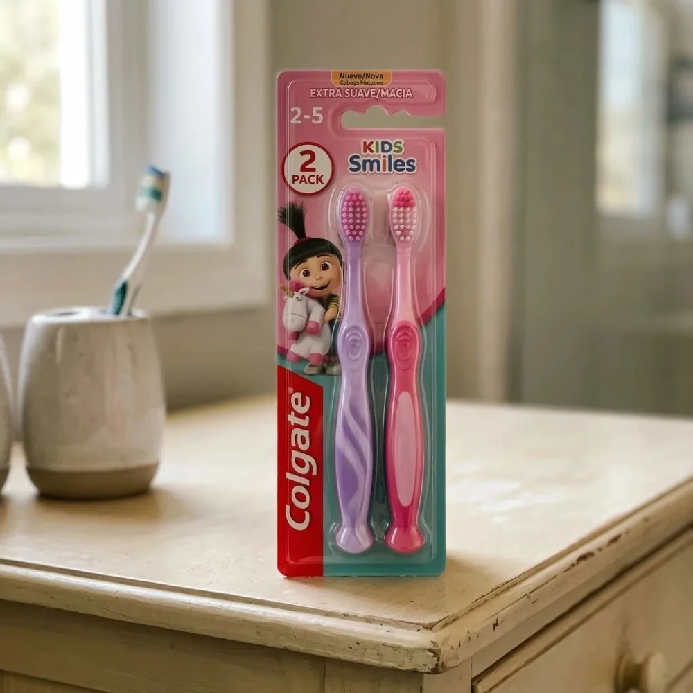 Cartela com duas escovas Colgate Kids Smiles de 2 a 5 anos, uma lilás e uma rosa, em pé sobre uma cômoda de madeira clara perto da janela